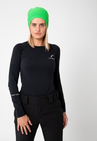 Green knit beanie with a textured weave. Model wears a black long-sleeve top and black high-waisted pants with a belt.