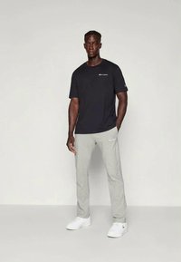 Black short-sleeve t-shirt with logo on chest, paired with light gray pants. Shoes are white. Simple and casual athletic wear.
