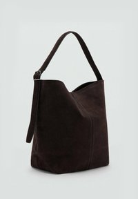 Bolso de mano de ante marrón con una forma estructurada, parte superior en ángulo y una sola correa de hombro ajustable. Diseño minimalista sin herrajes visibles.
