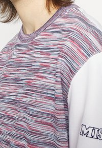 Camicia a maniche corte multicolore con un motivo testurizzato di strisce rosse, blu e bianche, con un'accenno bianco solido sulla manica.