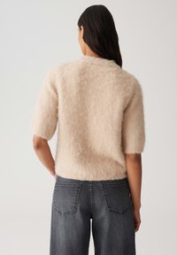 Hellbeige, flauschiger Strickpullover mit kurzen Ärmeln, kombiniert mit dunkelgrauen, weiten Jeans. Die Textur wirkt weich und leicht flauschig.