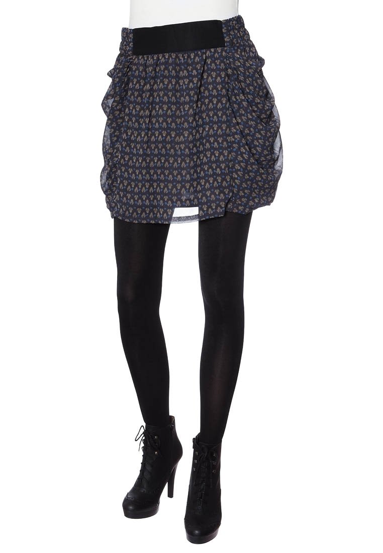 Falda corta negra y estampada con detalles plisados y una cinturilla ancha, combinada con medias negras y botas de tobillo con cordones.