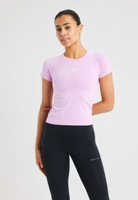 Ljusrosa tränings-t-shirt med korta ärmar och åtsittande design, kombinerad med svarta högmidjade leggings med logotypdetalj.
