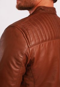Braune Lederjacke mit einem gesteppten Schulterdesign und glatter Textur. Die Passform ist tailliert mit dezenten Stichdetails.