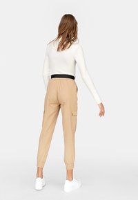 Beige cargobroek met een elastische tailleband en manchetten, voorzien van zijzakken. Draagt met een aansluitende witte lange mouwen top en witte sneakers.
