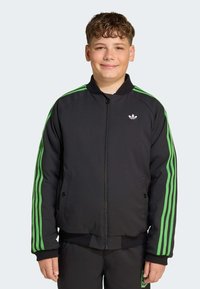Svart jacka med gröna ränder längs ärmarna, framzip, sidofickor och en liten vit logotyp på bröstet.