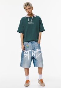 Green oversized t-shirt with "ERROR 404" text, light blue denim shorts, beige sneakers, and a colorful flower keychain. Text on shorts reads "ST WD."