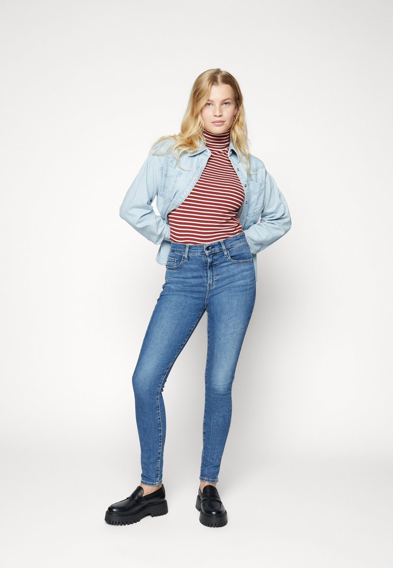 Blaue hochtaillierte Skinny-Jeans, kombiniert mit einem rot-weiß gestreiften Rollkragenpullover und einer hellen Jeansjacke. Schwarze Plateau-Lederloafers.