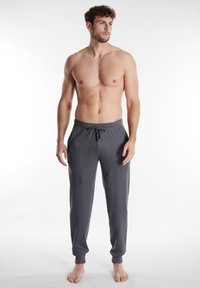 Pantaloni grigi a pullover con tessuto texturizzato, vita elastica e cordoncino. Orli a costine e tasche laterali. Modella in piedi a piedi nudi.