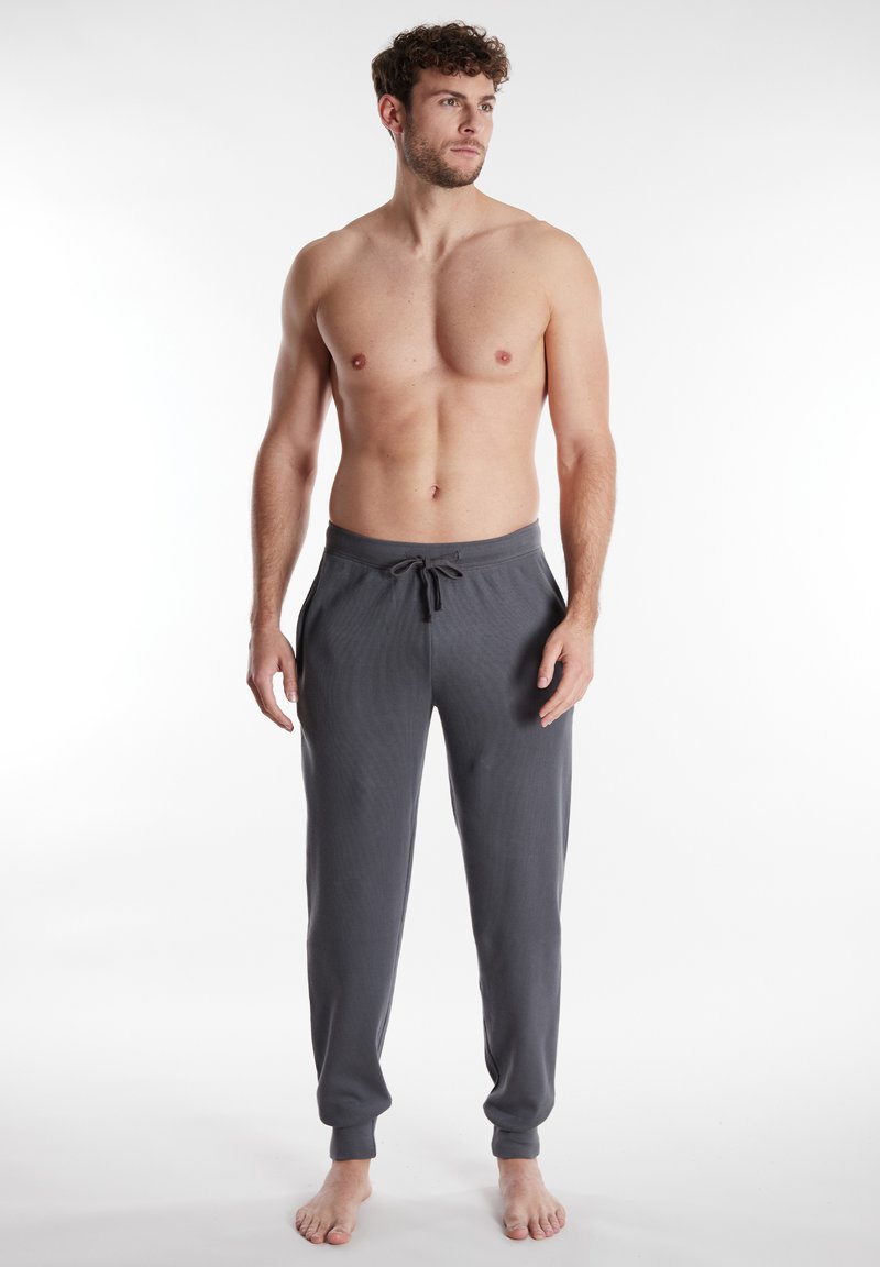 Pantaloni grigi a pullover con tessuto texturizzato, vita elastica e cordoncino. Orli a costine e tasche laterali. Modella in piedi a piedi nudi.