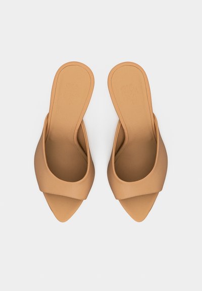 Paire de sandales beige ouvertes à bout pointu, à enfiler avec une large bride sur le dessus du pied, vue de dessus sur un fond uni.