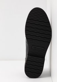 Chaussure noire avec une semelle en caoutchouc texturée, présentant un motif strié et un logo. Taille 37 indiquée à l'intérieur de la semelle.