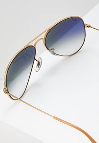 Ochelari de soare aviator aurii cu lentile degradé de culoare albastru închis, având un cadru subțire, o construcție ușoară și pernițe pentru nas ajustabile.