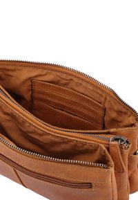 Brązowa skórzana torba z wieloma zamykanymi na zamek kieszeniami. Wnętrze charakteryzuje się gładką teksturą i miejscami na karty. Widoczne detale przeszycia.