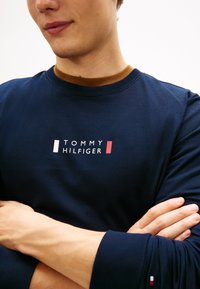 T-shirt a maniche lunghe blu navy con scollo rotondo, logo "TOMMY HILFIGER" bianco e rosso e dettaglio colorato sul collo.