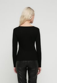 Top nero a maniche lunghe con scollo ampio e design aderente, abbinato a pantaloni in pelle neri che mostrano una texture liscia e opaca.