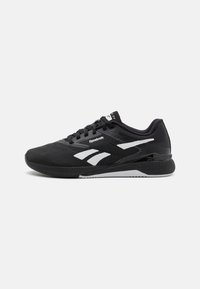 Mustad mustusportlikud kingad, millel on hingav võrkmaterjalist ülemine osa, valge Reebok logo, painduv tallapind ja tekstuuriga aktsendid parema haarde ja toe tagamiseks.