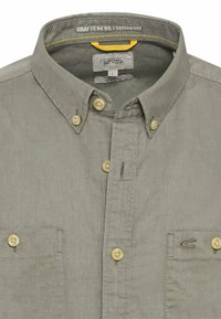 Lichtgrijs overhemd van zachte stof, voorzien van twee borstzakken, gele accenten in het stiksel en lichtbruine knopen.