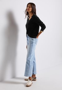 Svart v-ringad tröja, ljusblå högmidjade jeans och avslappnade sneakers. Outfitten förenar mjuka texturer och en avslappnad passform.