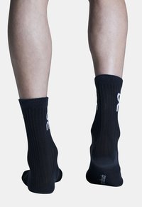 Chaussettes noires côtelées avec une texture tricotée, présentant un logo blanc à l'arrière. Longueur cheville, design ajusté pour un ajustement confortable.