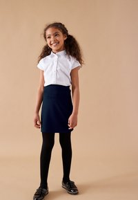 Biała koszula z krótkim rękawem zapinana na guziki, granatowa spódnica trapezowa, czarne rajstopy i czarne lakierowane buty z frędzlami. Prosty design.