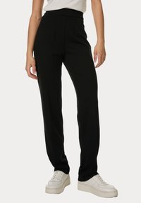 Svarta tapered-byxor med hög midja, veck fram och en slät tygkvalitet, kombinerat med vita sneakers för kontrast.