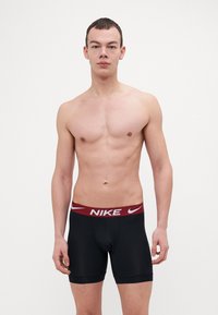 Fekete Nike boxer alsónadrág burgundi színű, rugalmas derékkal, amelyen fehér Nike logó található. Sima textúrájú és illeszkedő fazonú.
