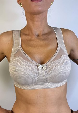 Sujetador inalámbrico beige con detalles de malla y encaje, tejido texturizado, tirantes anchos y un pequeño lazo en el centro.