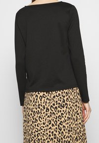 Černý top s dlouhým rukávem a kulatým výstřihem, v kombinaci s béžovou sukní s černým leopardím potiskem. Hladká textura, ležérní design.