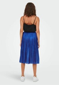 Sininen midi-hame, jossa on laskostus ja läpikuultava rakenne, yhdistetty mustaan ilmanhihaiseksi yläosaan. Asusteena valkoiset tennarit, mikä tuo esiin rentoa asustusta.