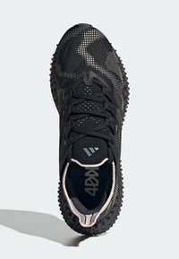 Zapatilla negra con suela texturizada, parte superior de punto, patrón de puntos blancos, cordones negros y un logo reflectante en la lengüeta, vista desde arriba.