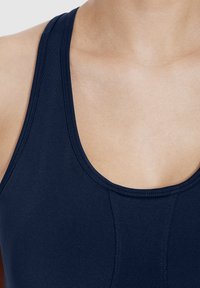 Camiseta deportiva sin mangas de color azul marino con un escote amplio y tejido suave y elástico. Las costuras visibles realzan la estructura y el ajuste.