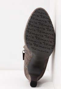 Botte marron à motif avec une tige en tissu texturé, fermeture éclair et semelle extérieure en caoutchouc noir arborant le logo Tamaris et la taille 37.