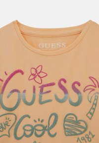 Ferskenfarvet bomulds t-shirt med flerfarvet grafisk tekst og design, herunder en blomst, palmetræ og hjerter, med rund halsudskæring.