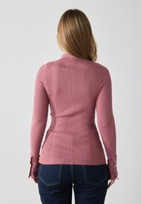 Ribbestrikket genser i myk rosa med lange ermer, en tettsittende silhuett og knapper på ermene. Laget av elastisk stoff for komfort.