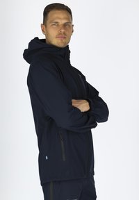 Marineblaue wasserdichte Jacke mit Kapuze, ausgestattet mit Reißverschlusstaschen und elastischen Bündchen. Hergestellt aus leichtem, glattem Stoff.