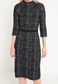 Svart och vit stickad klänning med ett strukturerat mönster, tre fjärdedelsärmar och en åtsittande midja, som faller till mitten av vaden.
