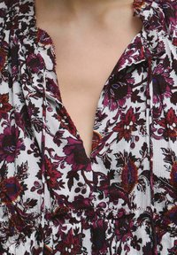 Vestito floreale con scollo a V, maniche corte e dettagli arricciati. I colori includono bianco, viola intenso e tocchi di rosso. Tessuto strutturato.