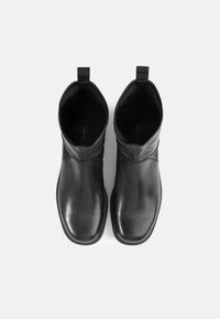 Botas de tobillo de cuero negro con una textura suave, puntera redondeada y paneles laterales elásticos. Cuenta con lengüetas para facilitar el calzado.