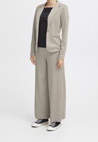 Beige rutigt kavaj och matchande vida byxor med en svart topp under. Svarta sneakers fulländar outfiten.