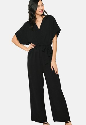 Zwarte jumpsuit met een V-hals, korte mouwen en een strikceintuur in de taille. Heeft wijde pijpen en een zachte, gestructureerde stof.