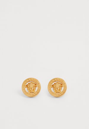 Brincos redondos em tom de ouro com um design de cabeça de leão em relevo, apresentando uma banda padronizada à volta da borda. Acabamento metálico suave.