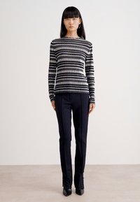 Schwarz-weißer gestreifter Langarmtop mit rundem Halsausschnitt, kombiniert mit maßgeschneiderten dunklen Hosen und spitzen schwarzen High Heels. Glattes Material; taillierte Passform.