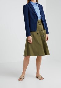 Navy double-breasted blazer with peak lapels, paired with a high-waisted olive green skirt featuring front buttons and side pockets. Brown sandals.