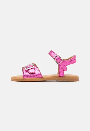 Sandali metallici rosa con cinturino regolabile alla caviglia, due fibbie sulla parte anteriore, suola piatta e superficie liscia.