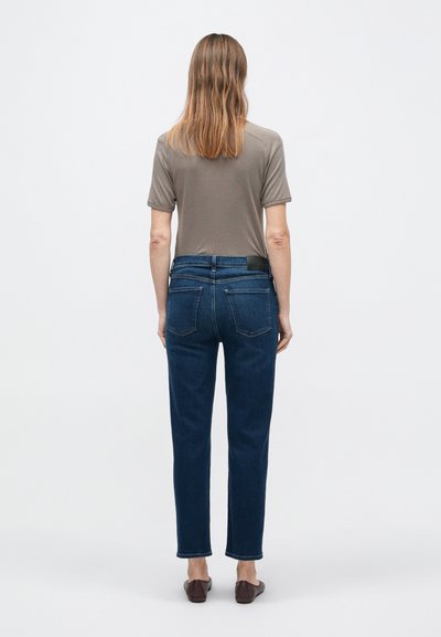 Sötétkék farmernadrág egyenes szárú, sima textúrájú, két hátsó zsebbel. Szürke rövid ujjú felsővel párosítva.