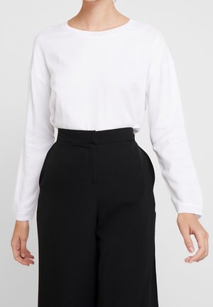 Weißes Langarmoberteil mit Rundhalsausschnitt, kombiniert mit hoch sitzenden schwarzen Hosen. Beide Kleidungsstücke haben eine glatte Textur und ein schlichtes Design.