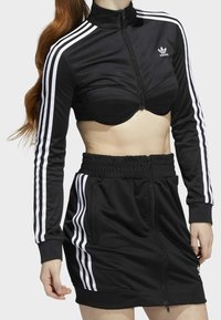Black athletic outfit featuring a cropped zip jacket with white stripes and matching high-waisted skirt, both made of smooth fabric.