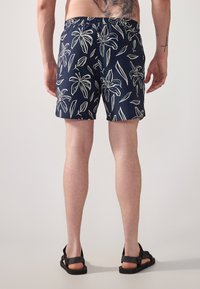 Marine svømmebukser laget av lett stoff, med et hvitt blomstermønster. Elastisk midje og sideslisser for komfort og bevegelighet.