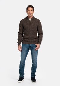 Bruin geribbelde trui met een halve rits kraag, gecombineerd met een blauwe spijkerbroek en zwarte sneakers. De trui heeft een gestructureerde, spikkelachtige uitstraling.